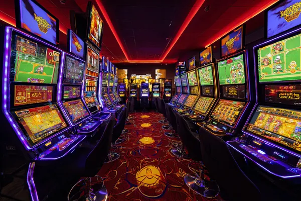 A woman smiling by bright slot machines showing lucky symbols, showcasing the exciting slot offerings at 21GAME.